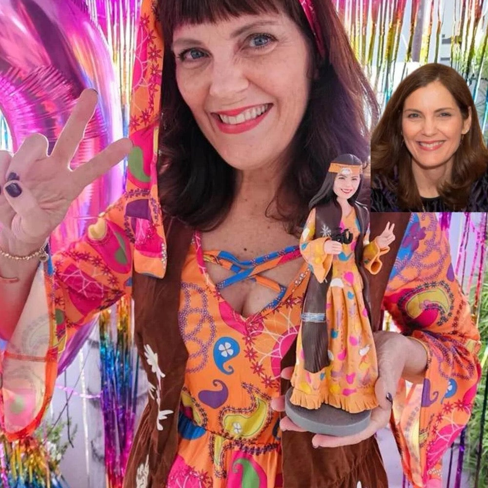 A woman in a colorful costume holding a custom figurine that resembles a cake topper. The figurine has a second head showing a different angle of the design.