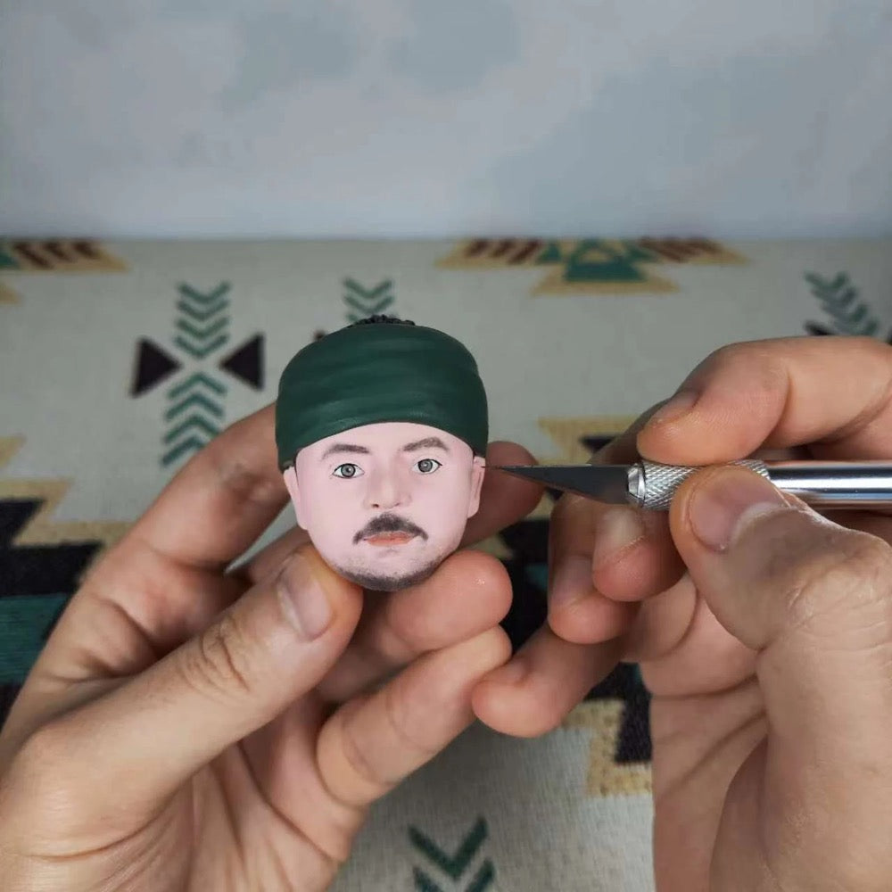 Handcrafted custom military bobblehead in progress, featuring a detailed face and artist applying finishing touches.