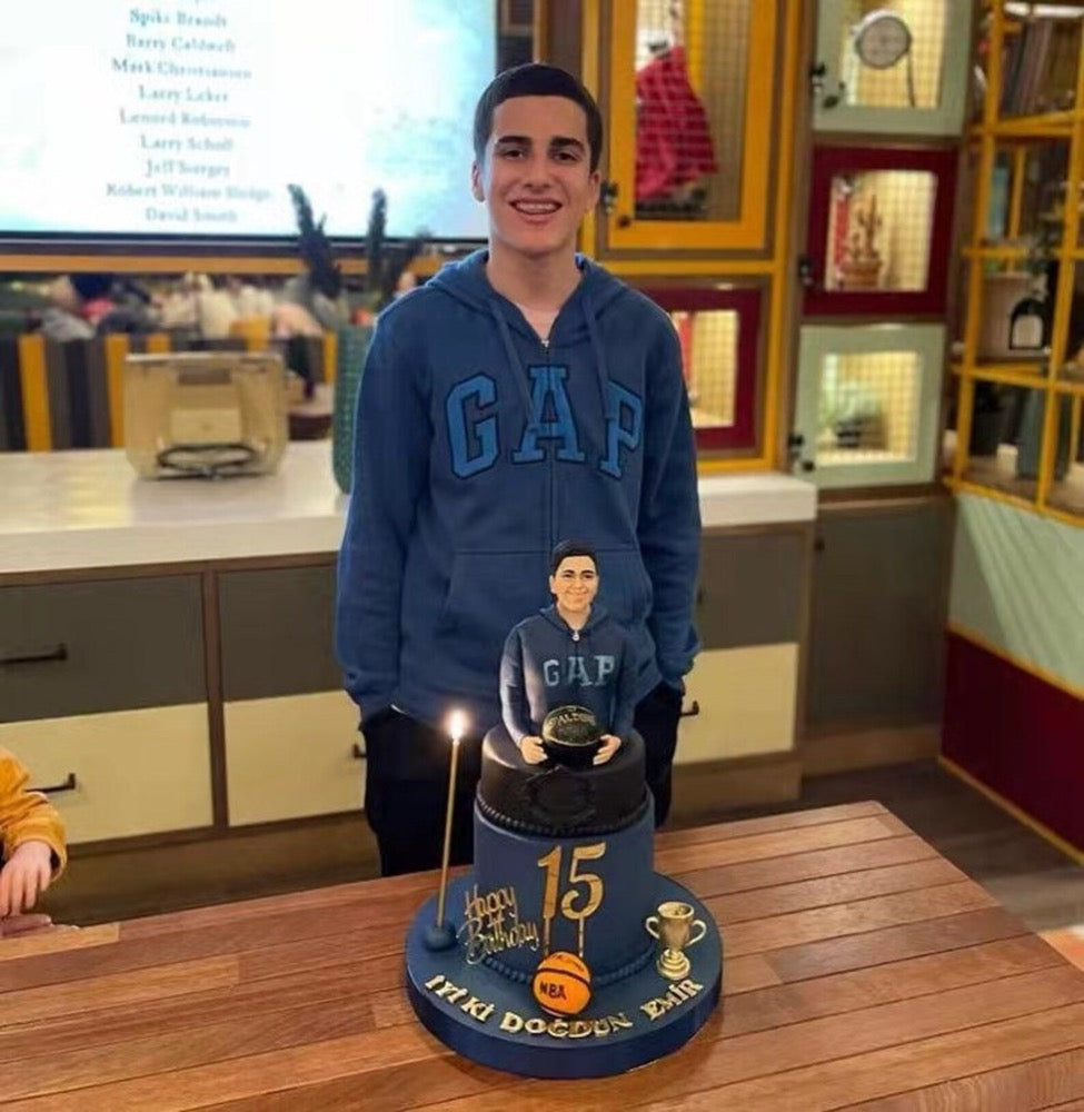 Person wearing a blue GAP hoodie with a birthday cake featuring a small figure and '15' on a wooden table.
