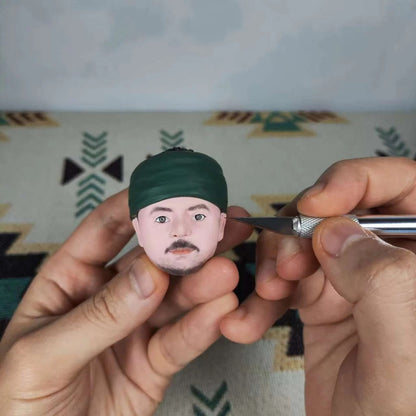 Handcrafted custom military bobblehead in progress, featuring a detailed face and artist applying finishing touches.